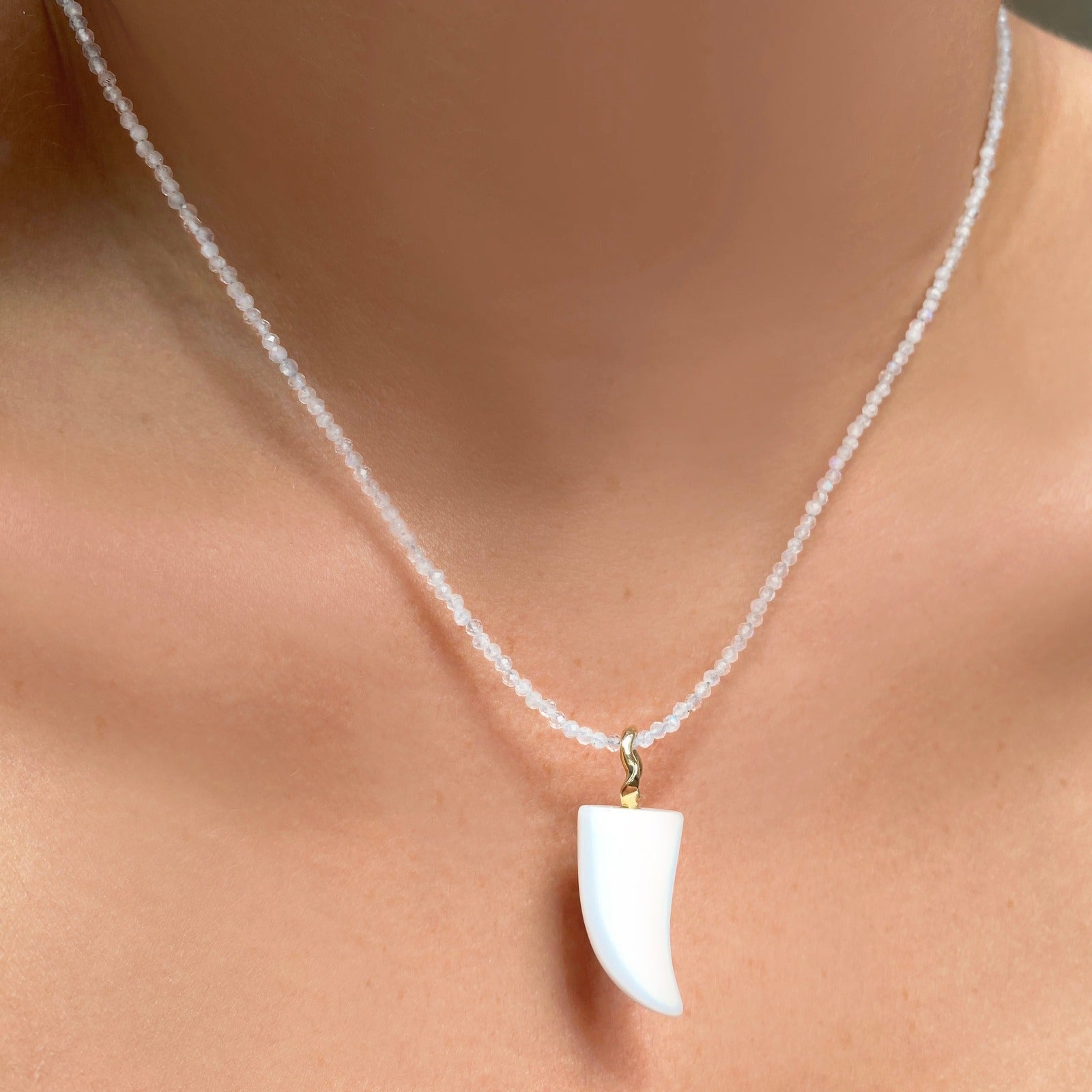 White agate horn charm. Styled on a neck hanging from a beaded necklace.