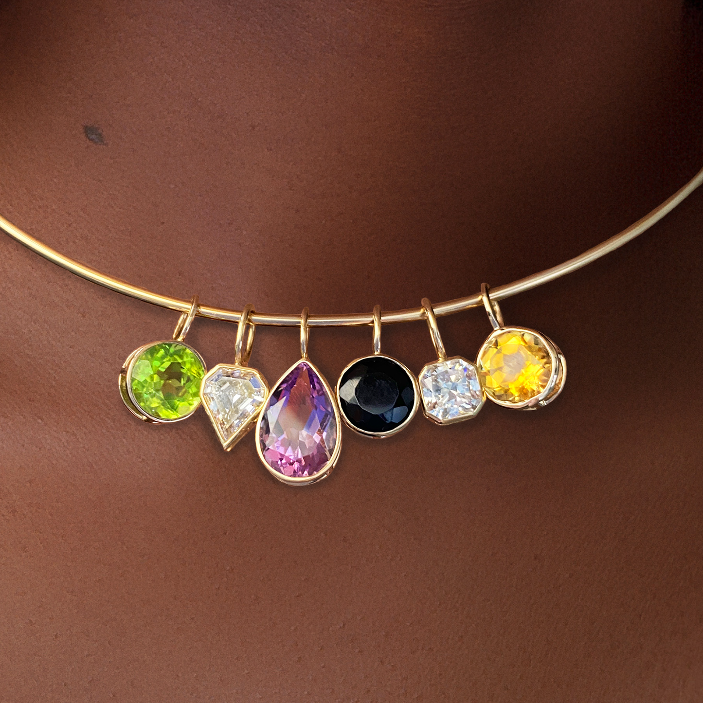 Various 14k gold shaped solitaire charms styled on a neck with the wire choker necklace