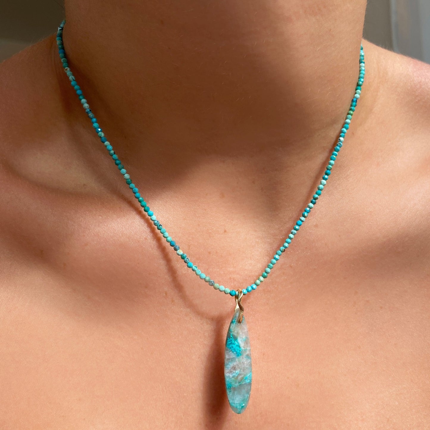 Chrysocolla in Quartz Surfboard Charm. Styled on a neck hanging from a beaded necklace.