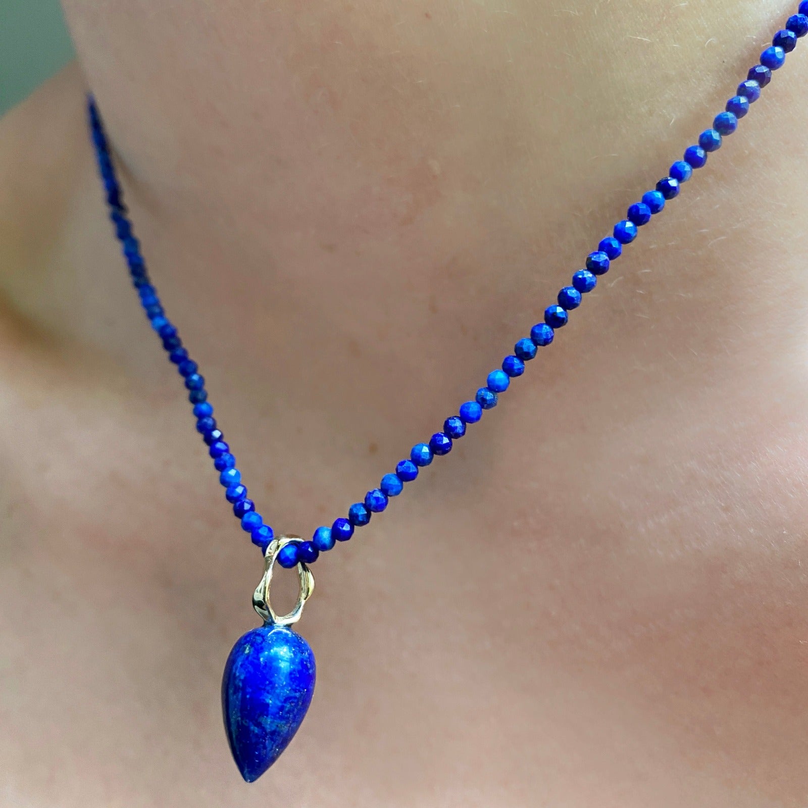 Lapis acorn drop charm. Styled on a neck hanging from a beaded necklace.