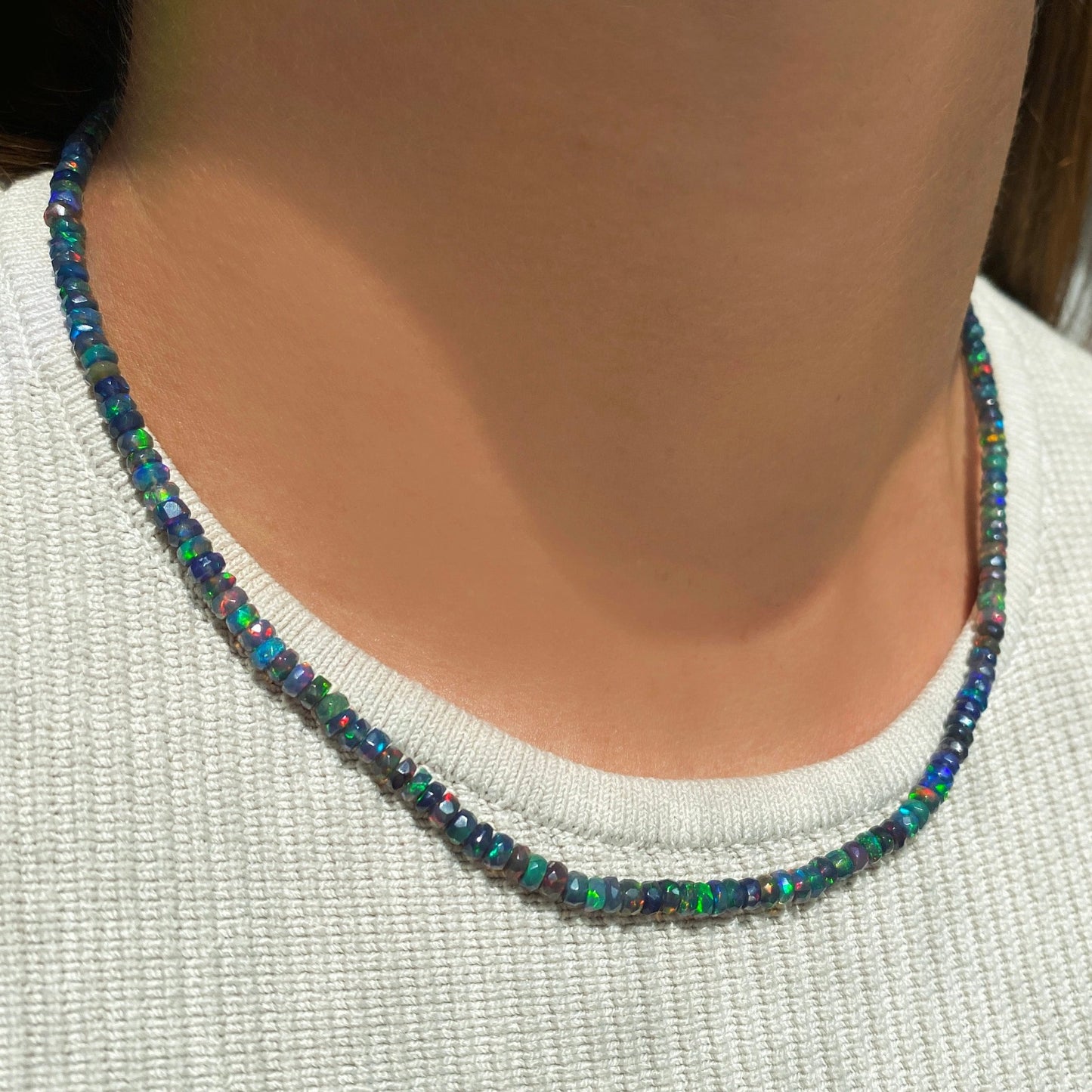Shimmering beaded necklace made of faceted opals in shades of black, green, and blue on a gold linking ovals clasp. 