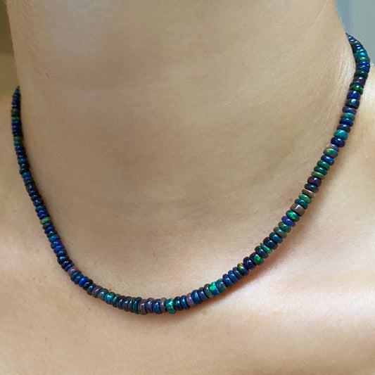 Shimmering beaded necklace made of smooth opal rondels in shades of black, navy, and green on a slim gold lobster clasp.