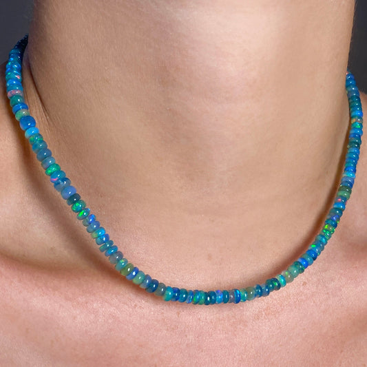 Shimmering beaded necklace made of smooth opal rondels in shades of blue, teal, and green on a slim gold oval clasp. 