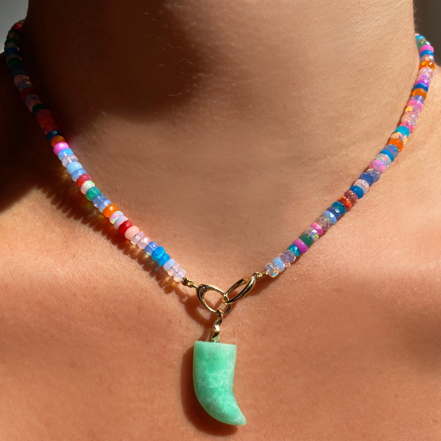 Shimmering beaded necklace made of faceted opals in shades of fiery blues, yellows, teal, and purple on a gold linking ovals clasp. Styled on a neck layered with an amazonite horn charm.
