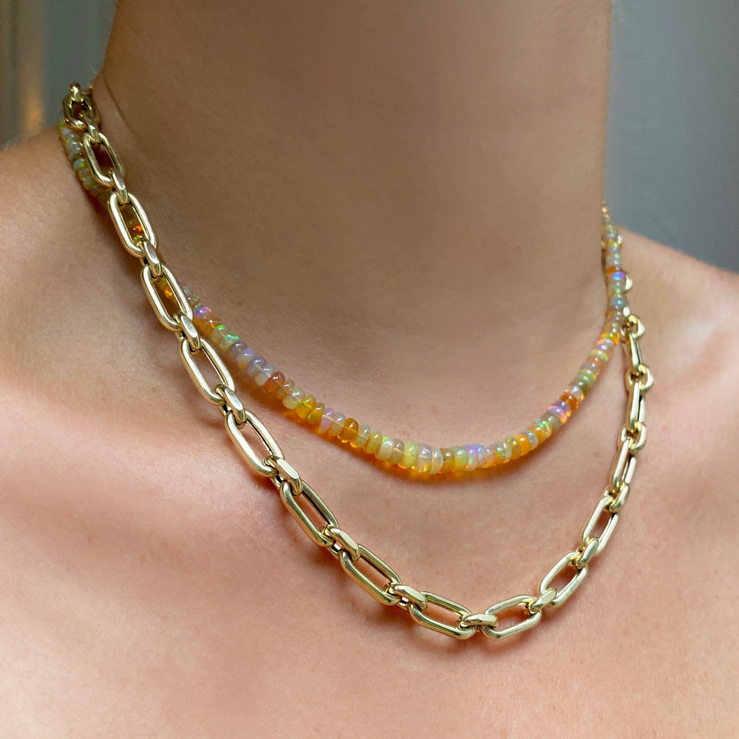 Shimmering beaded necklace made of faceted opals in shades of yellow, orange, and clear opals on a gold linking ovals clasp. Styled on a neck layered with the diamond cut link chain necklace.