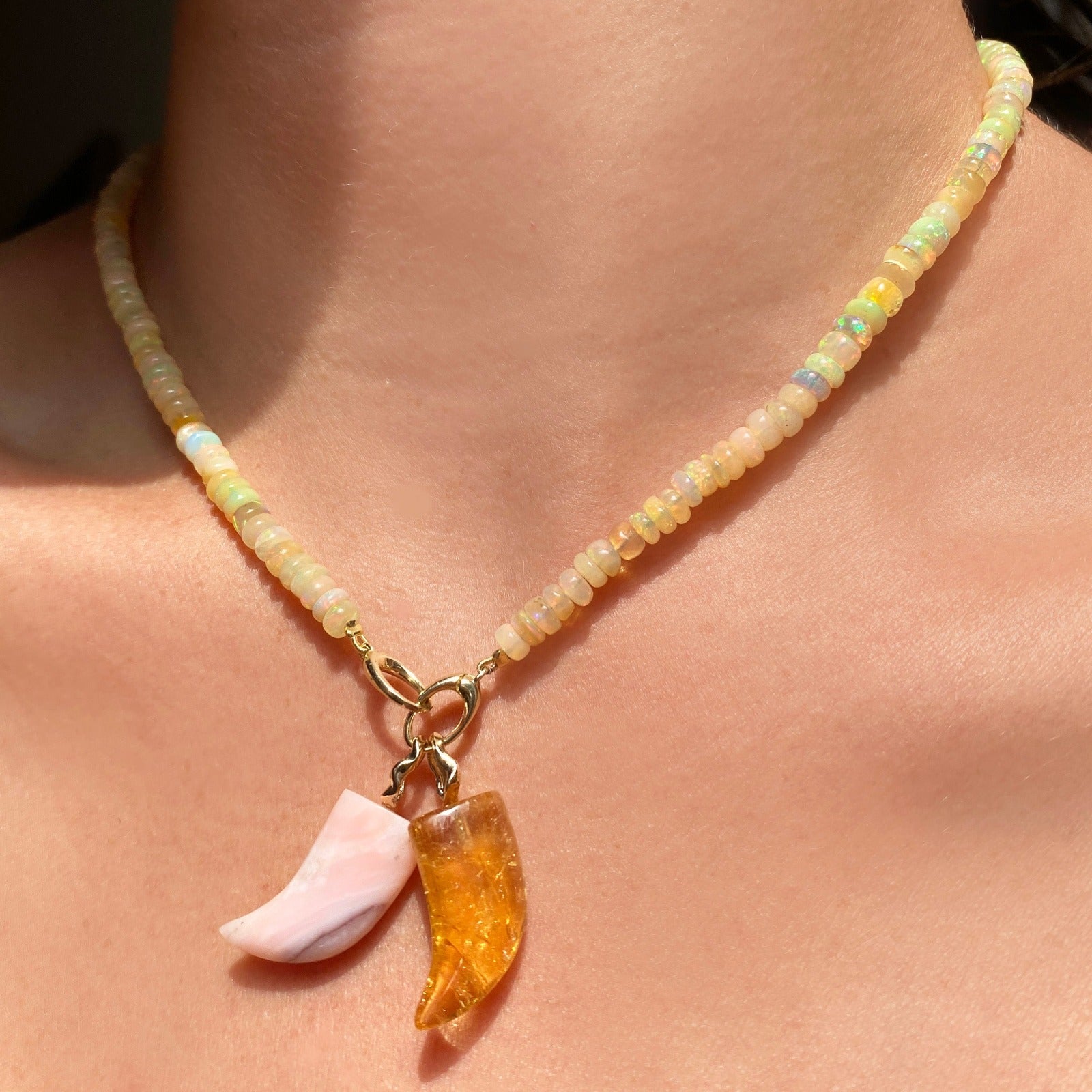 Pink opal horn charm. Styled on a neck with one other horn charm hanging from oval clasps of a beaded necklace. 
