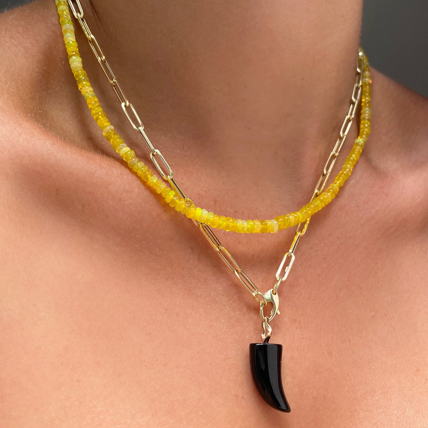 Black agate horn charm. Styled on a neck hanging from the lobster clasp of a chunky paperclip chain necklace.