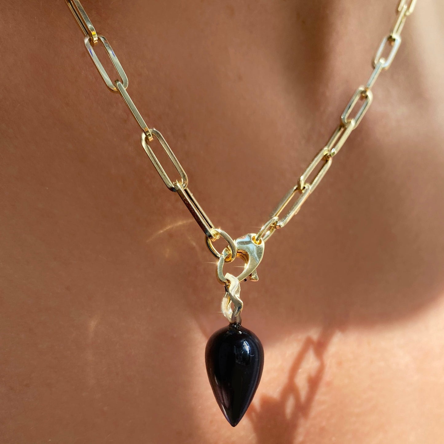 Black agate acorn drop charm. Styled on a neck hanging from the lobster clasp of a chunky paperclip chain necklace