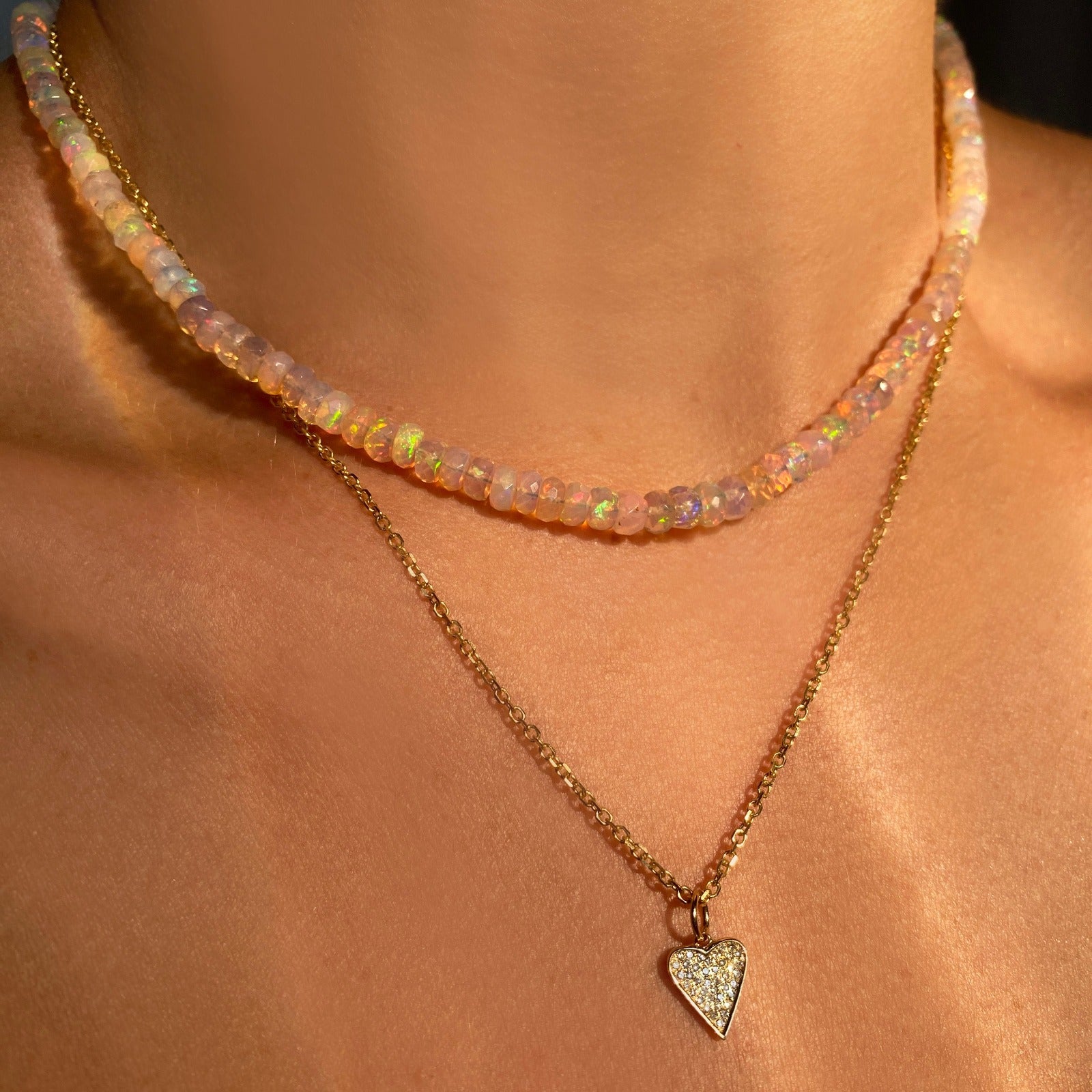 Shimmering beaded necklace made of faceted opals in shades of clear-light pink on a gold linking ovals clasp. Styled on a neck layered with a medium diamond pave heart charm.