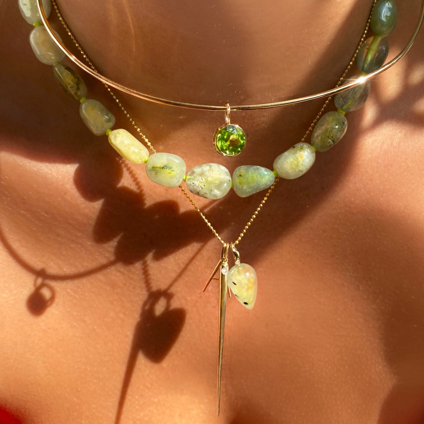 Prehnite acorn drop charm. Styled on a neck hanging from a beaded necklace with the A letter charm, quill spike charm, and round solitaire charm.