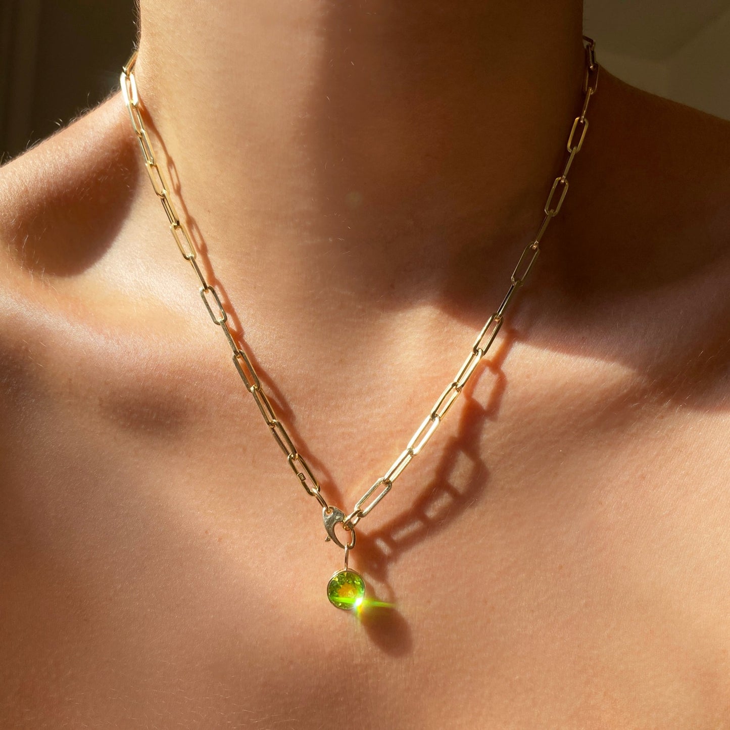 14k gold Peridot Round Solitaire Charm. Styled on a neck hanging from the lobster clasp of a paperclip chain necklace.