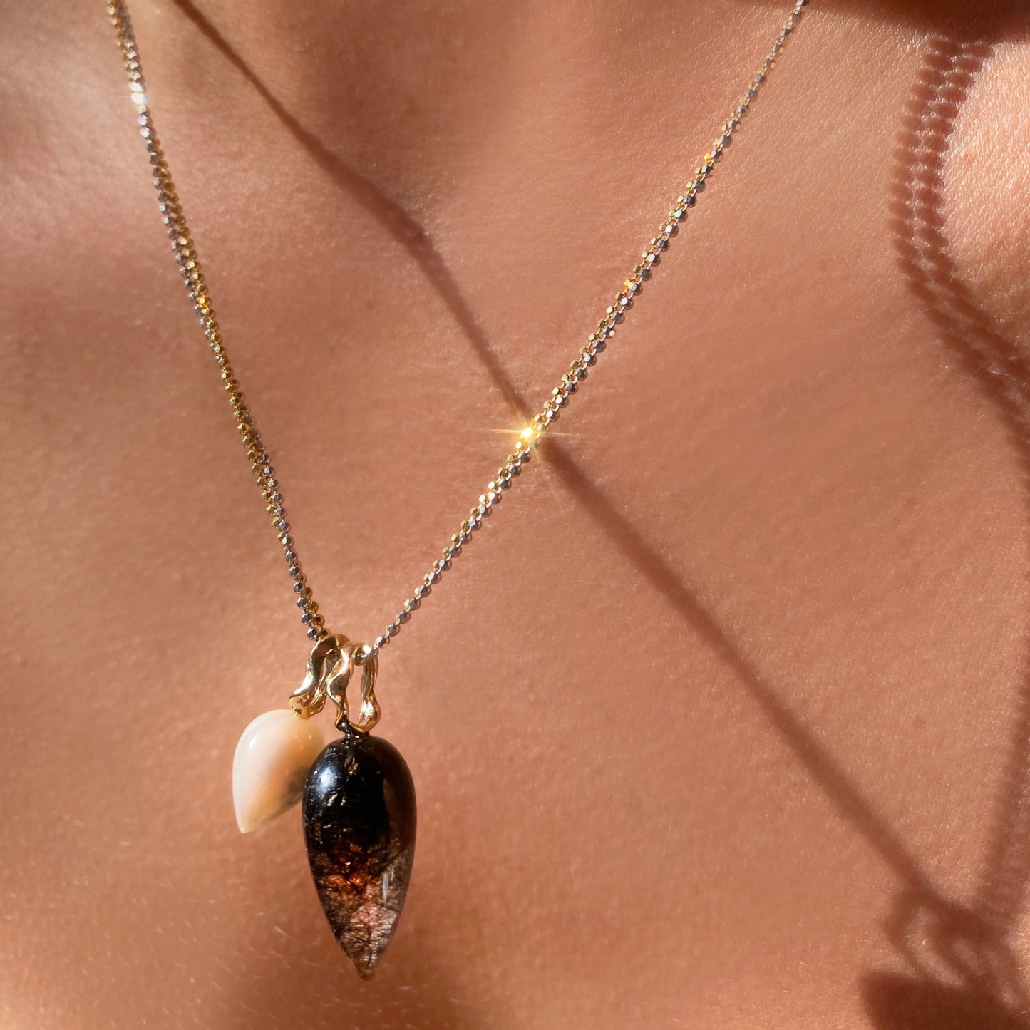 Mother of Pearl acorn drop charm. Styled on a neck with one other acorn drop charm hanging from a diamond cut bead chain necklace.
