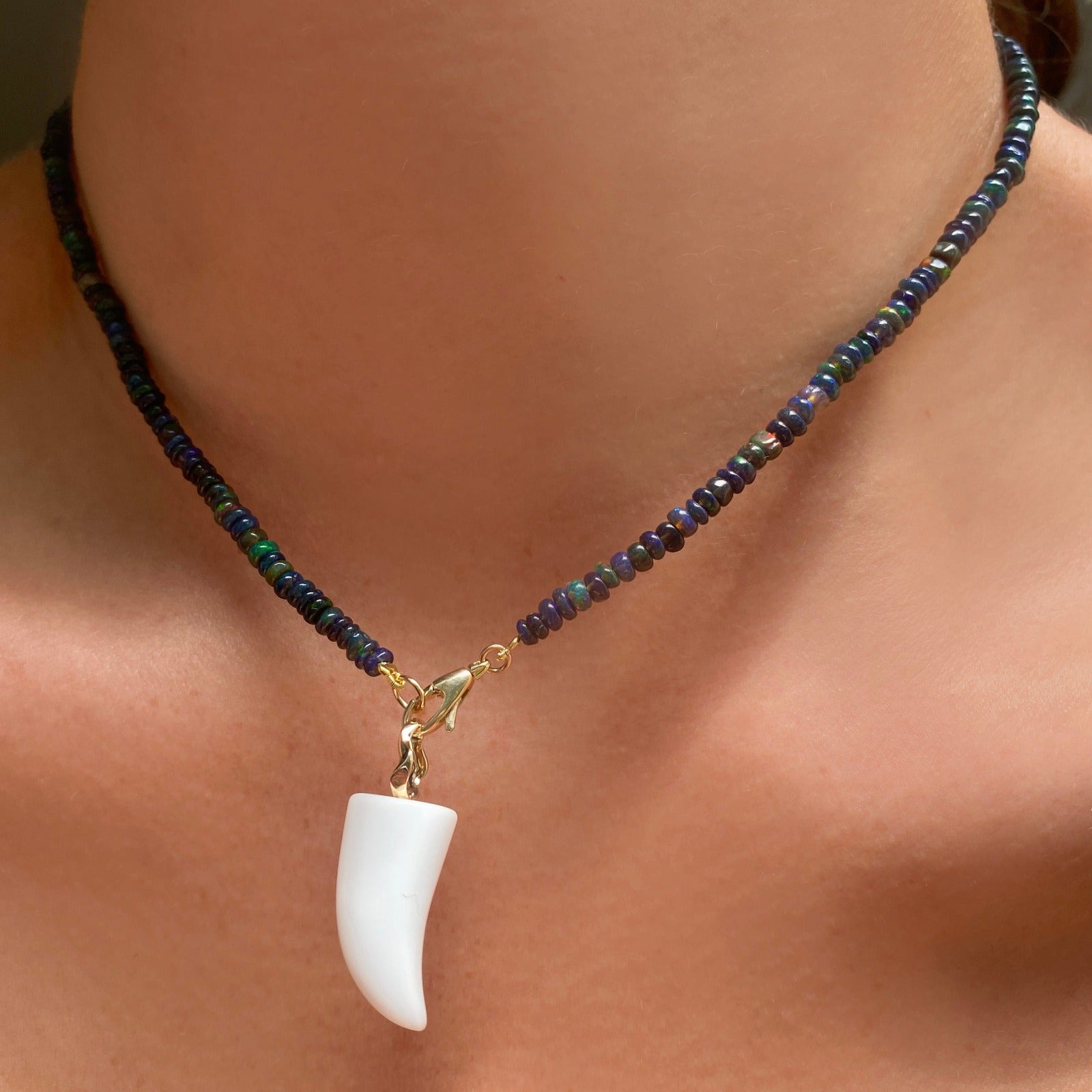 White agate horn charm. Styled on a neck hanging from the lobster clasp of a beaded necklace.