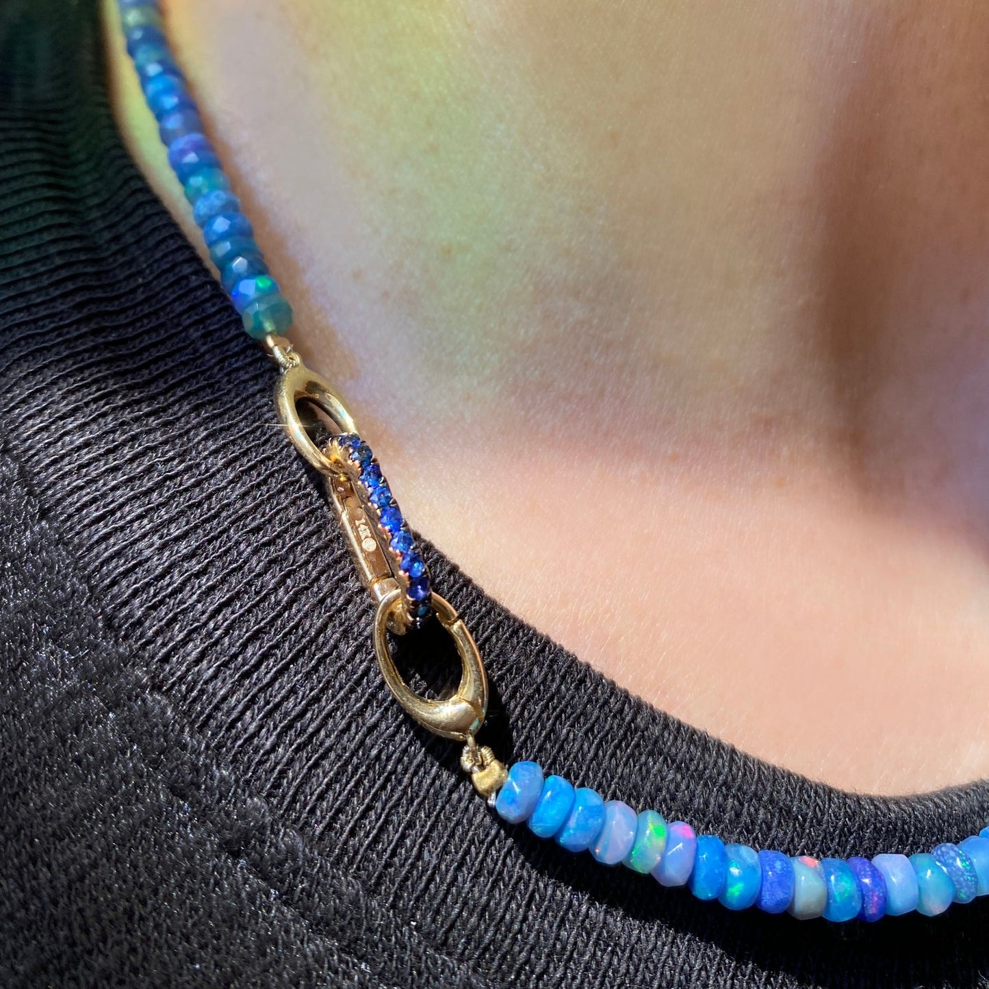 14k yellow gold oval locking charm with blue stones. Styled on a neck locked onto oval clasps of a beaded necklace.