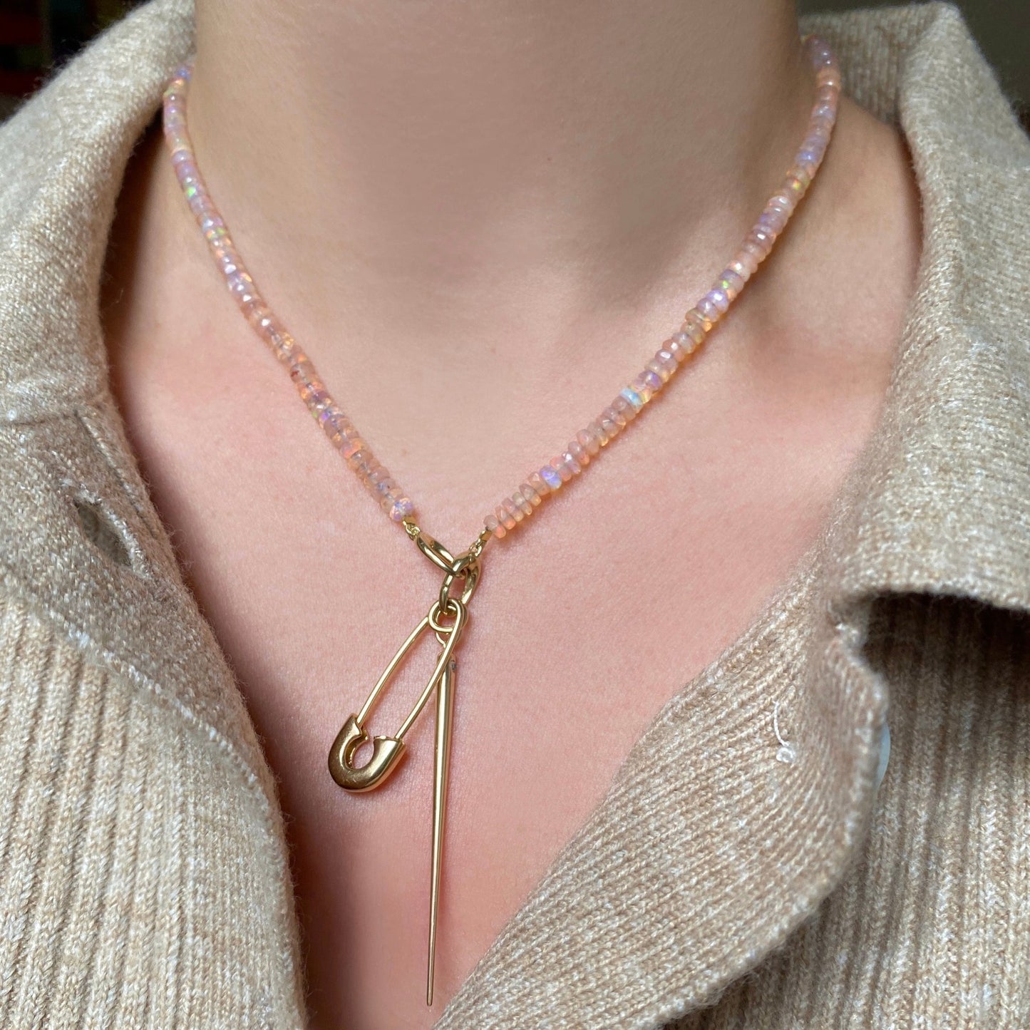 Shimmering beaded necklace made of faceted opals in shades of clear-light pink on a gold linking ovals clasp. Styled on a neck layered with the safety pin and quill spike charms.