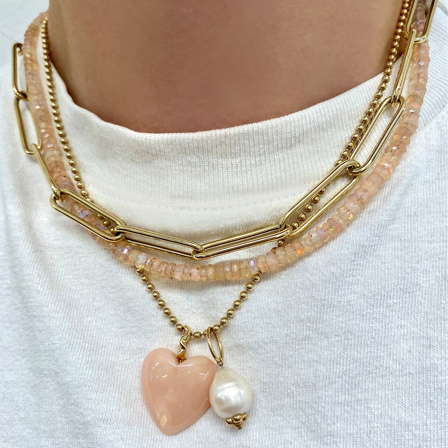 Shimmering beaded necklace made of faceted opals in shades of clear-light pink on a gold linking ovals clasp. Styled on a neck layered with the bead chain necklace, paperclip chain necklace, an mini baroque pearl charm.