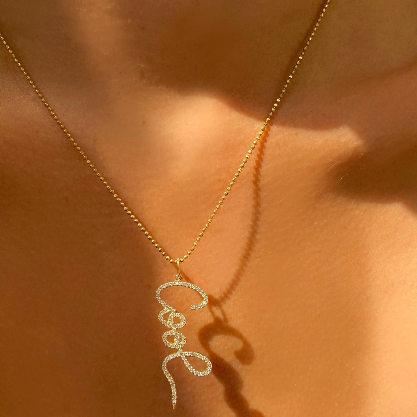 14k gold Diamond Cut Bead Chain Necklace. Styled on a neck with a pave graffiti "Cool" charm