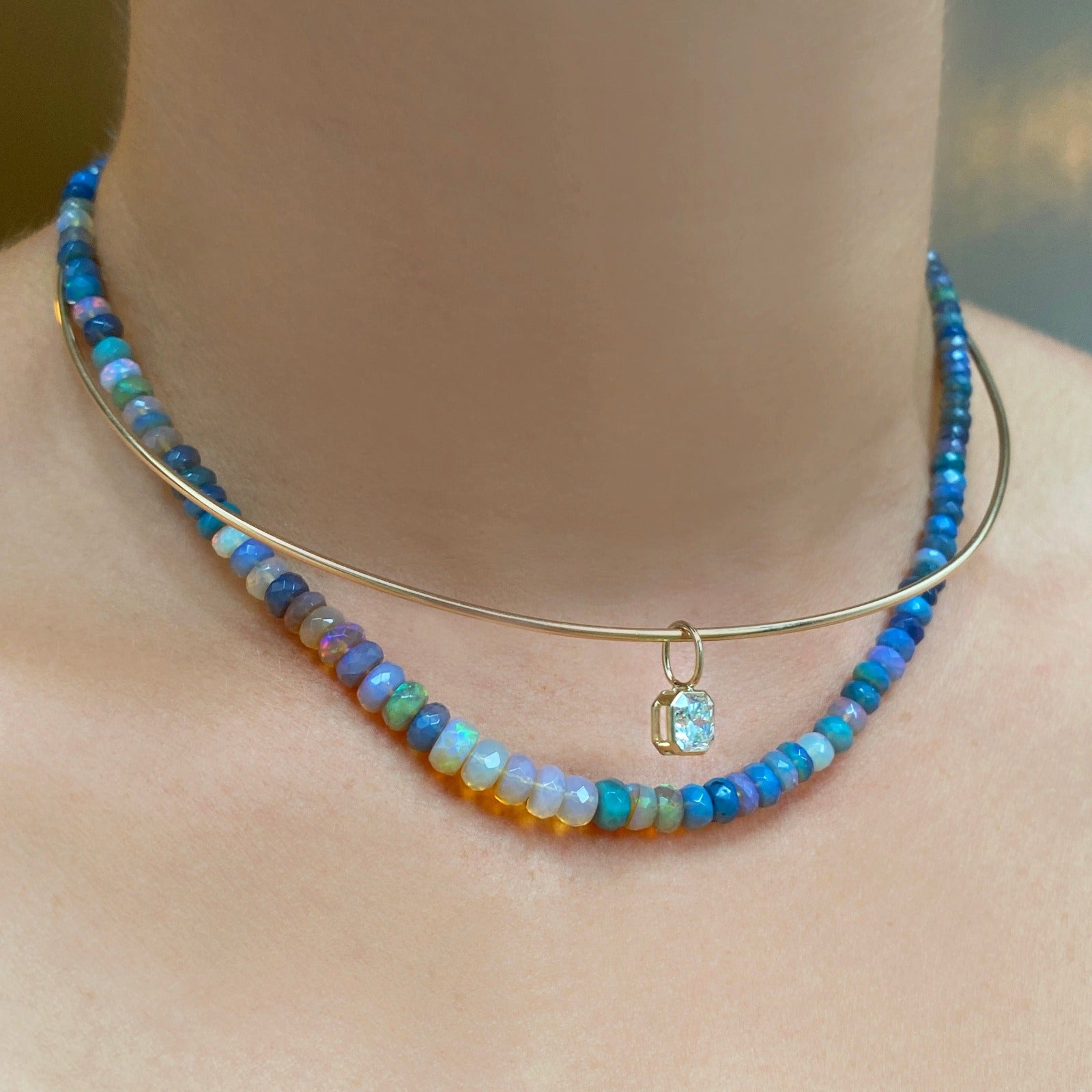 Shimmering beaded necklace made of faceted opals in shades of light blue, light purple, yellow, white, and clear on a gold linking ovals clasp. Styled on a neck with the wire choker necklace and aquila cut diamond solitaire charm.