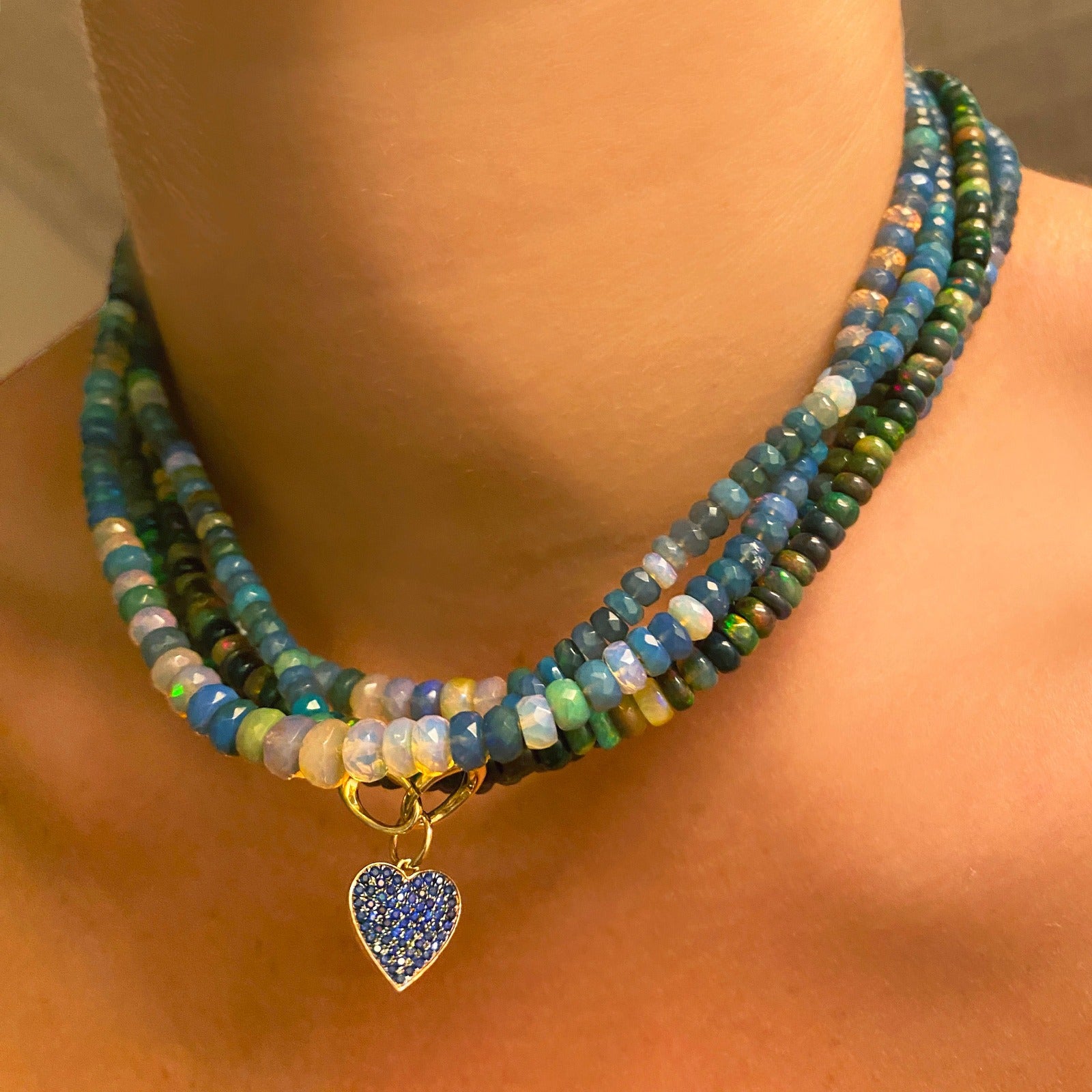 Shimmering beaded necklace made of faceted opals in shades of light blue, light purple, yellow, white, and clear on a gold linking ovals clasp. Styled on a neck with the medium pave heart charm.