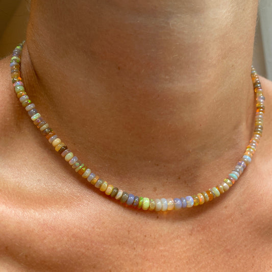 Shimmering beaded necklace made of smooth opal rondels in shades of light yellow, light orange, white, and brown on a slim gold lobster clasp. 