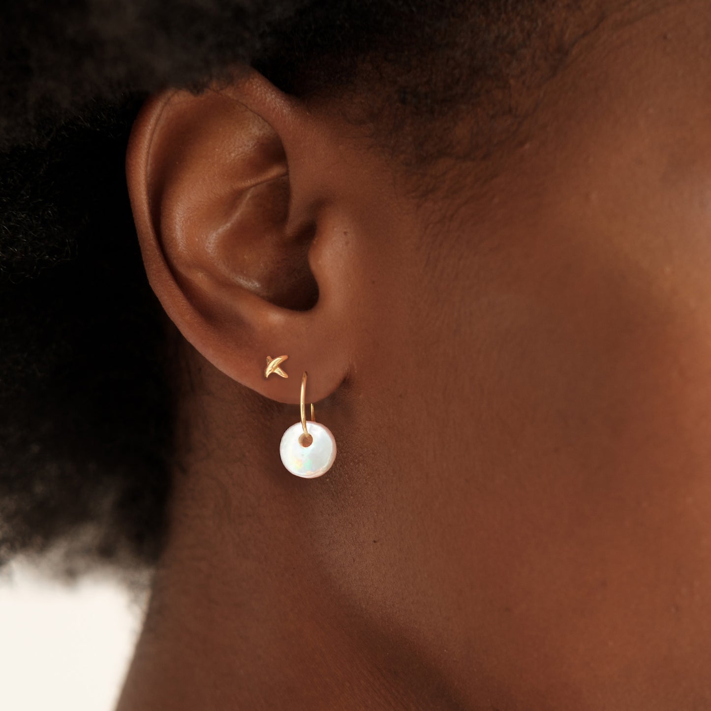 14k gold Stitch Stud Earrings styled on a ear with a coin pearl hoop