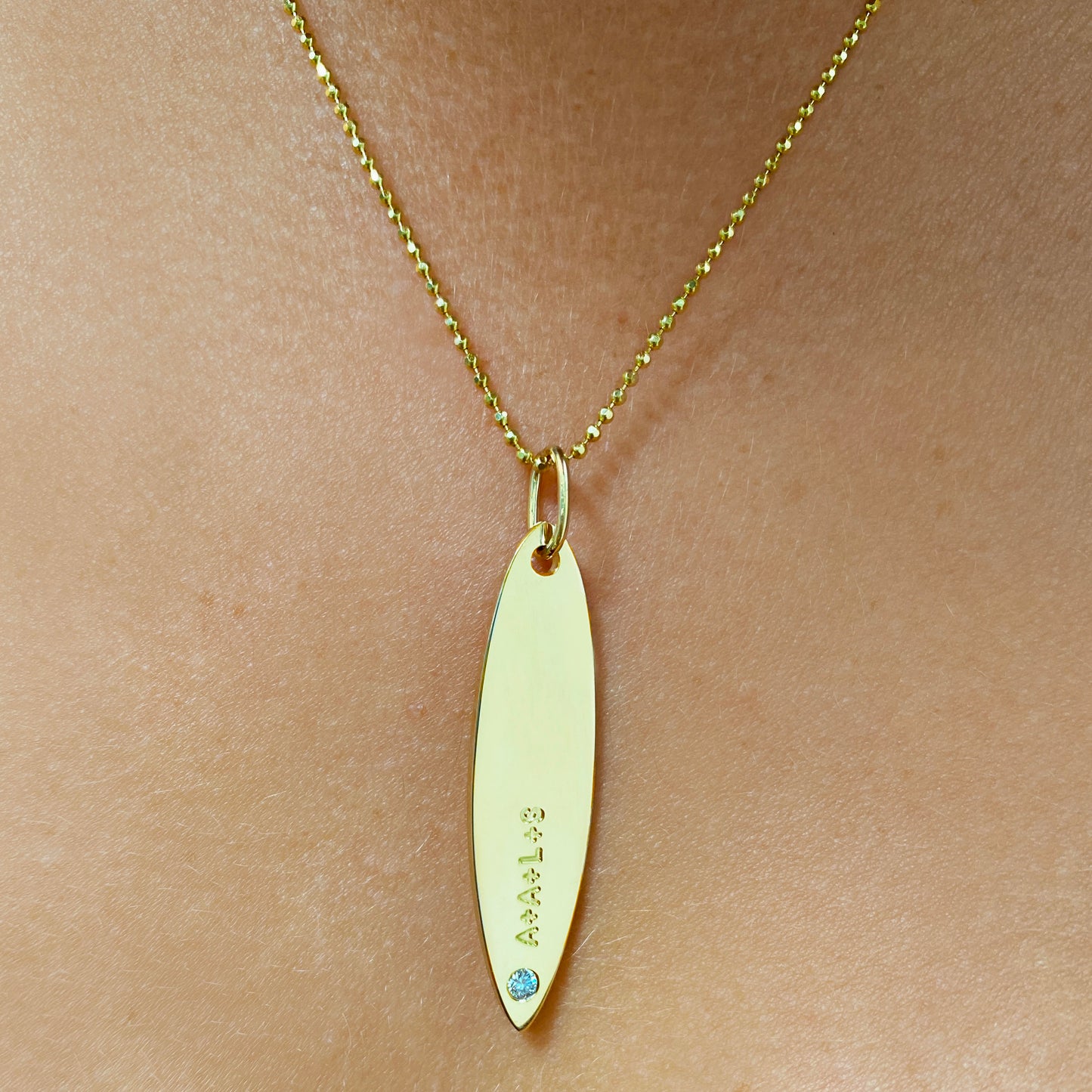 14k gold surfboard charm lock with A+A+L+S engraved and diamond. Styled on a neck hanging from a diamond cut bead necklace.