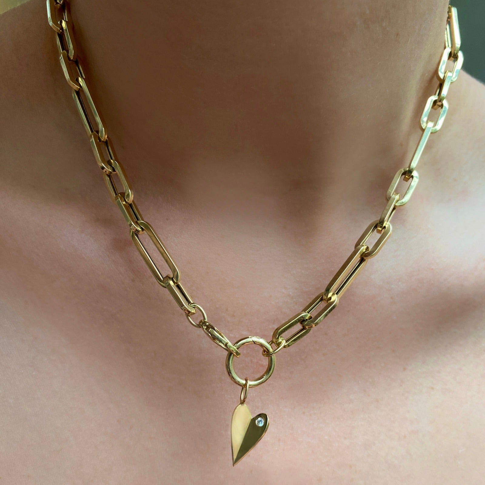 14k gold 13mm Plain Round Charm Lock. Styled on a neck with a folded heart charm hanging from oval clasps of a chunky paperclip chain necklace.