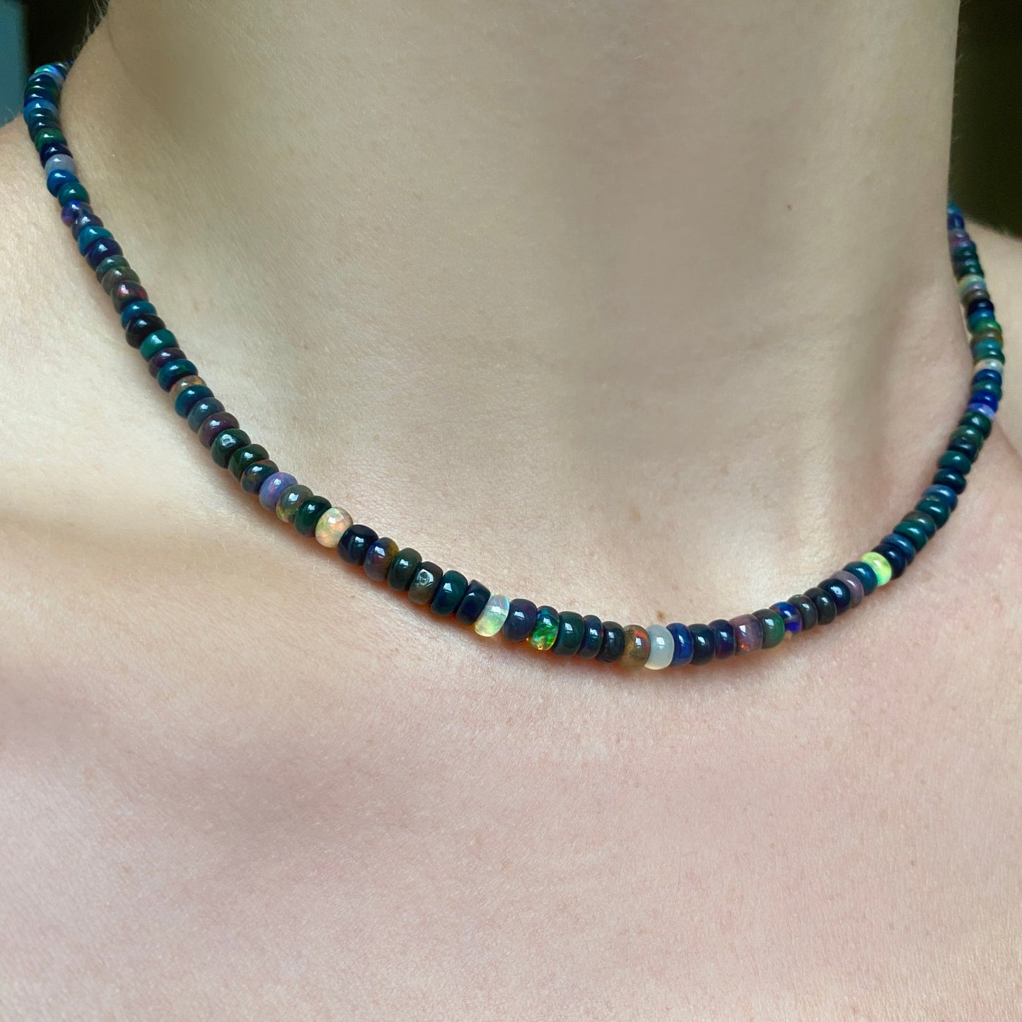 Shimmering beaded necklace made of smooth opal rondels in shades of black, dark green, navy, and clear on a slim gold lobster clasp. 