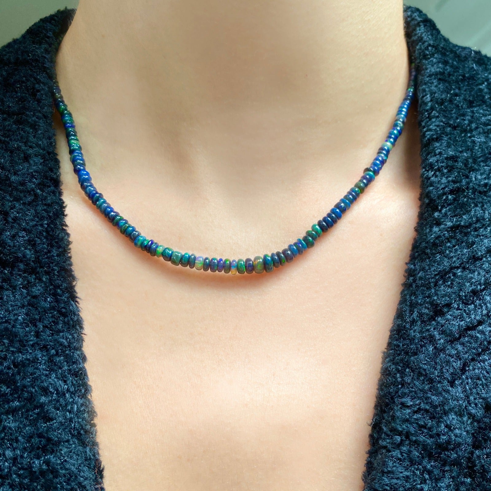 Shimmering beaded necklace made of smooth opal rondels in shades of black, navy, and green on a slim gold lobster clasp.