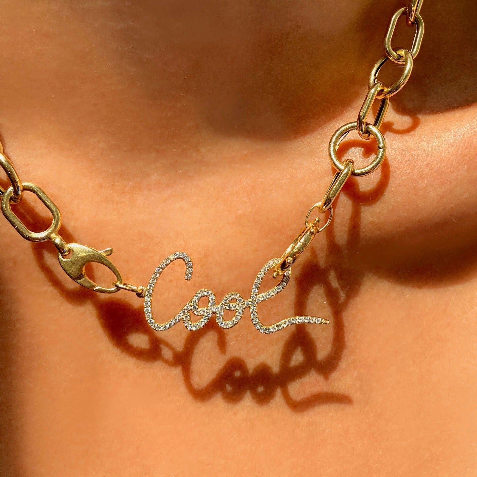14k gold Pavé Graffiti 'Cool' Charm. Styled on a neck hanging from the lobster clasps of a chain necklace 