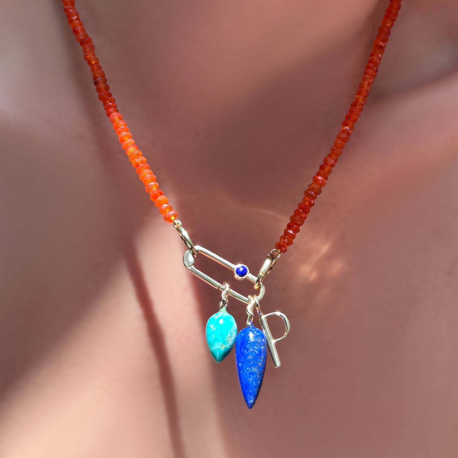 AMANDA PEARL faceted carnelian necklace with paperclip charm lock with lapis, and letter P charm, long lapis drop charm, and chrysocolla drop charm hanging on a model's neck.