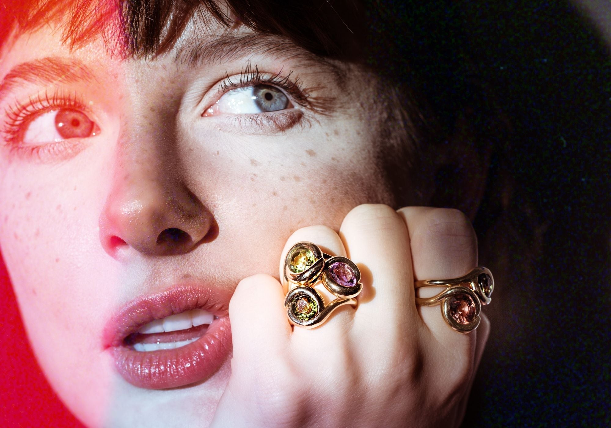 A close up of a model wearing an AMANDA PEARL recycled 14K amethyst and two green tourmaline molten knot rings on one finger. On another finger she wears a pink tourmaline and green tourmaline 14K molten knot ring.