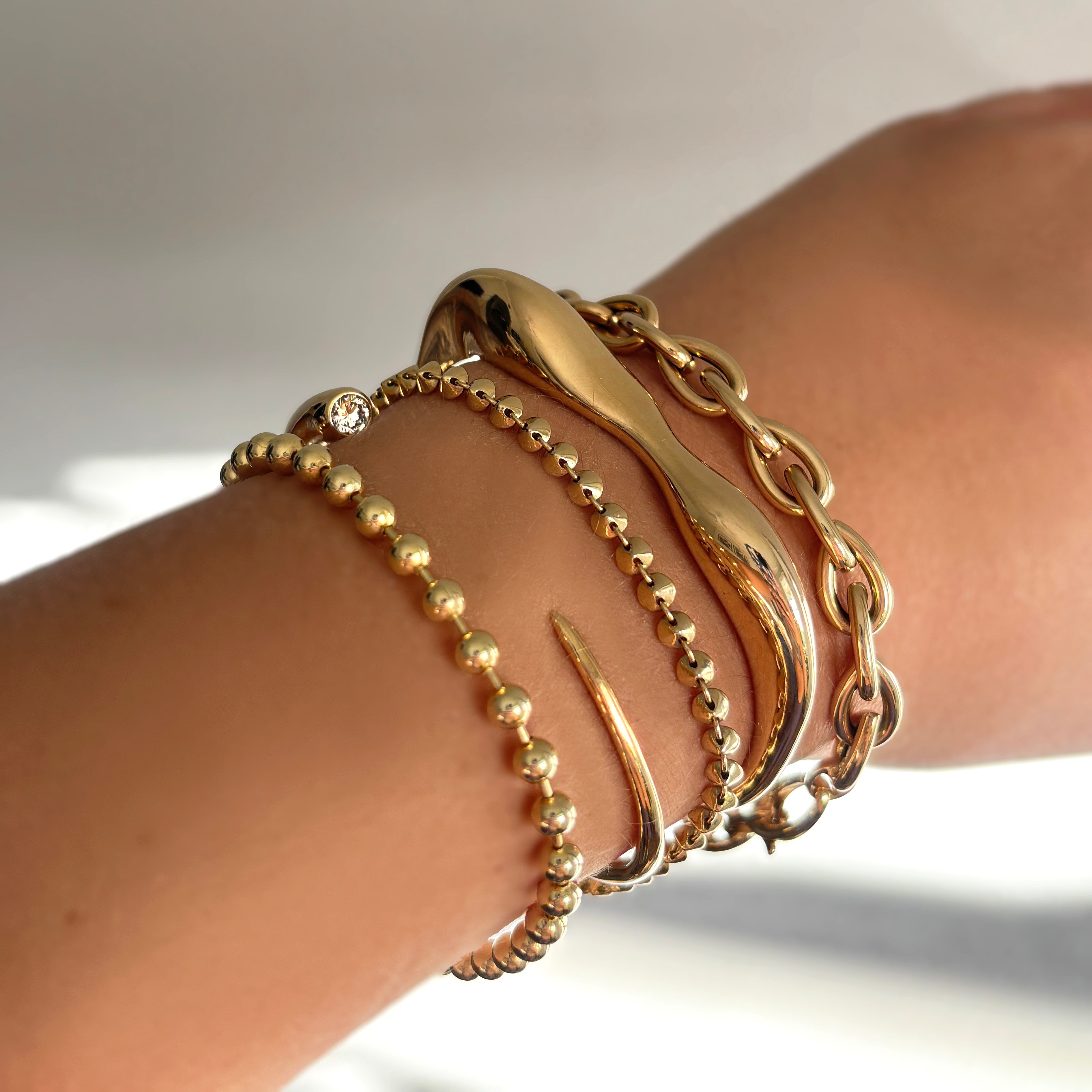 Bracelets and Anklets: Full Pavé 14K gold ripple cuffs styled on a wrist with quill bypass rings and ripple rings