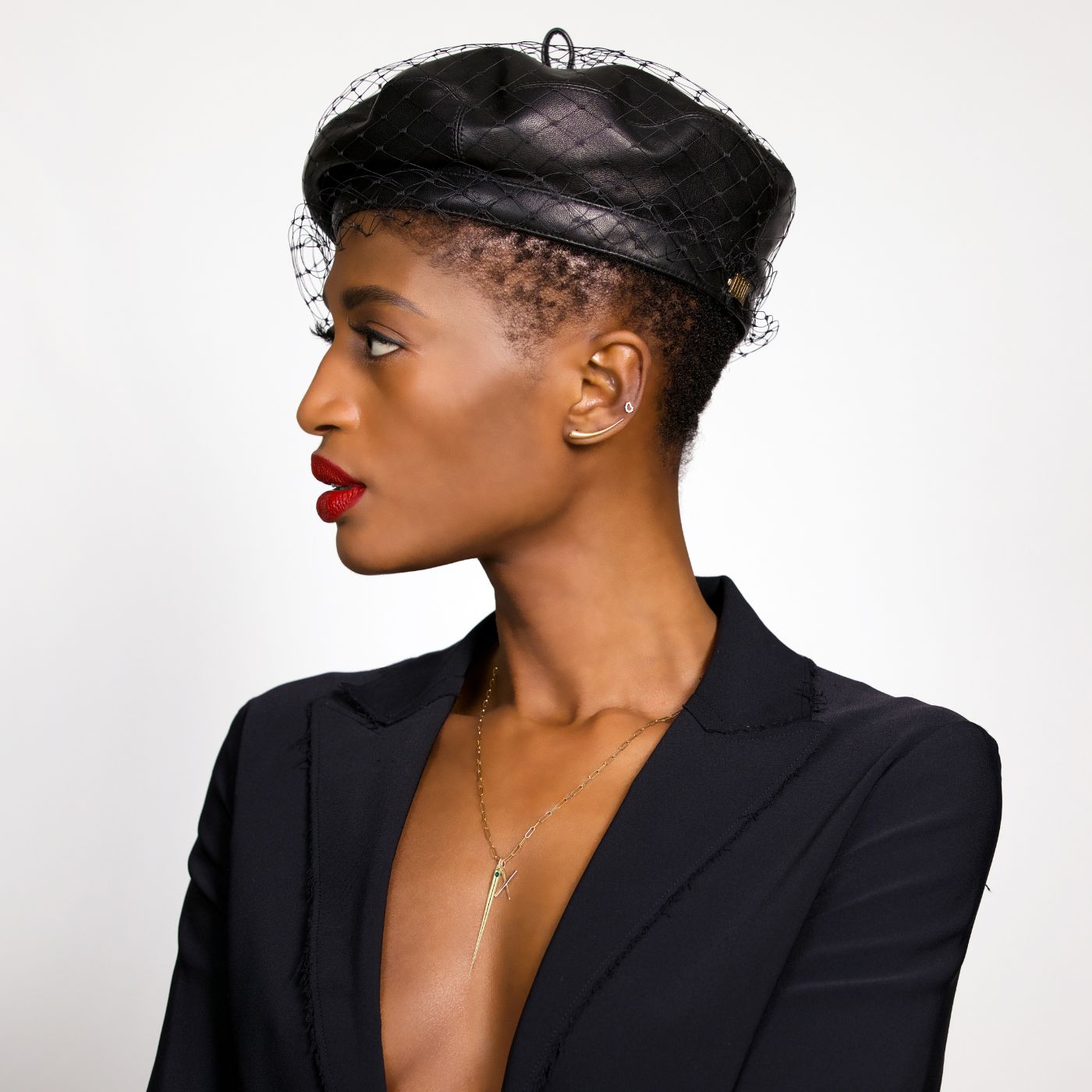 Model in red lipstick, chic black blazer and beret with veil, wearing AMANDA PEARL Quill Climbers, Quill Spike Charm, and Quill Leter Charm.