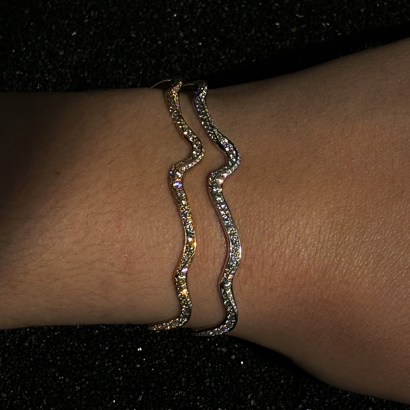 Two full diamond pavé ripple cuffs stacked on the wrist over a black sequin dress.