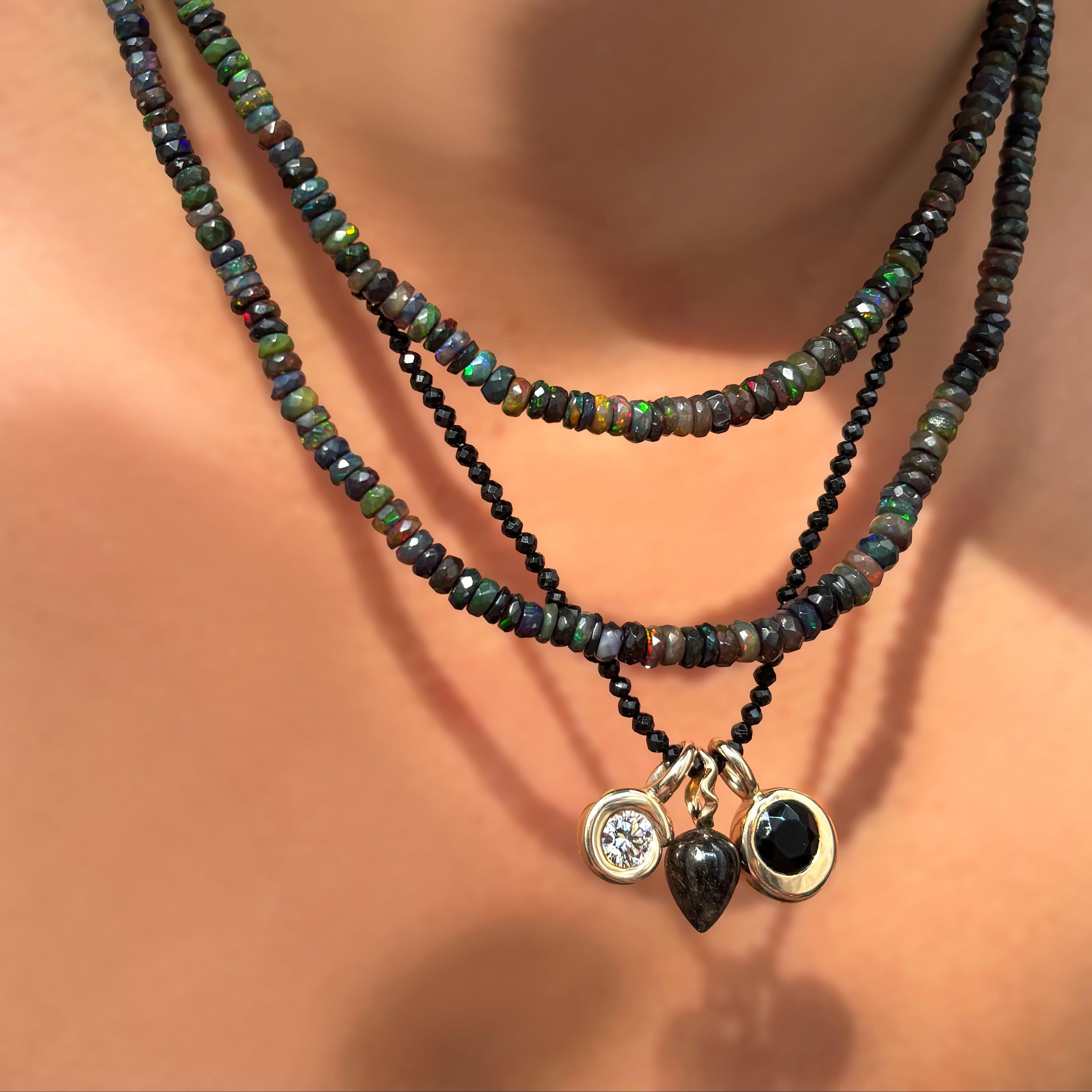 Shimmering beaded necklace made of faceted opal rondels in shades of Bright Blue on a gold oval linking clasp, styled on a neck layered with a chain and charm