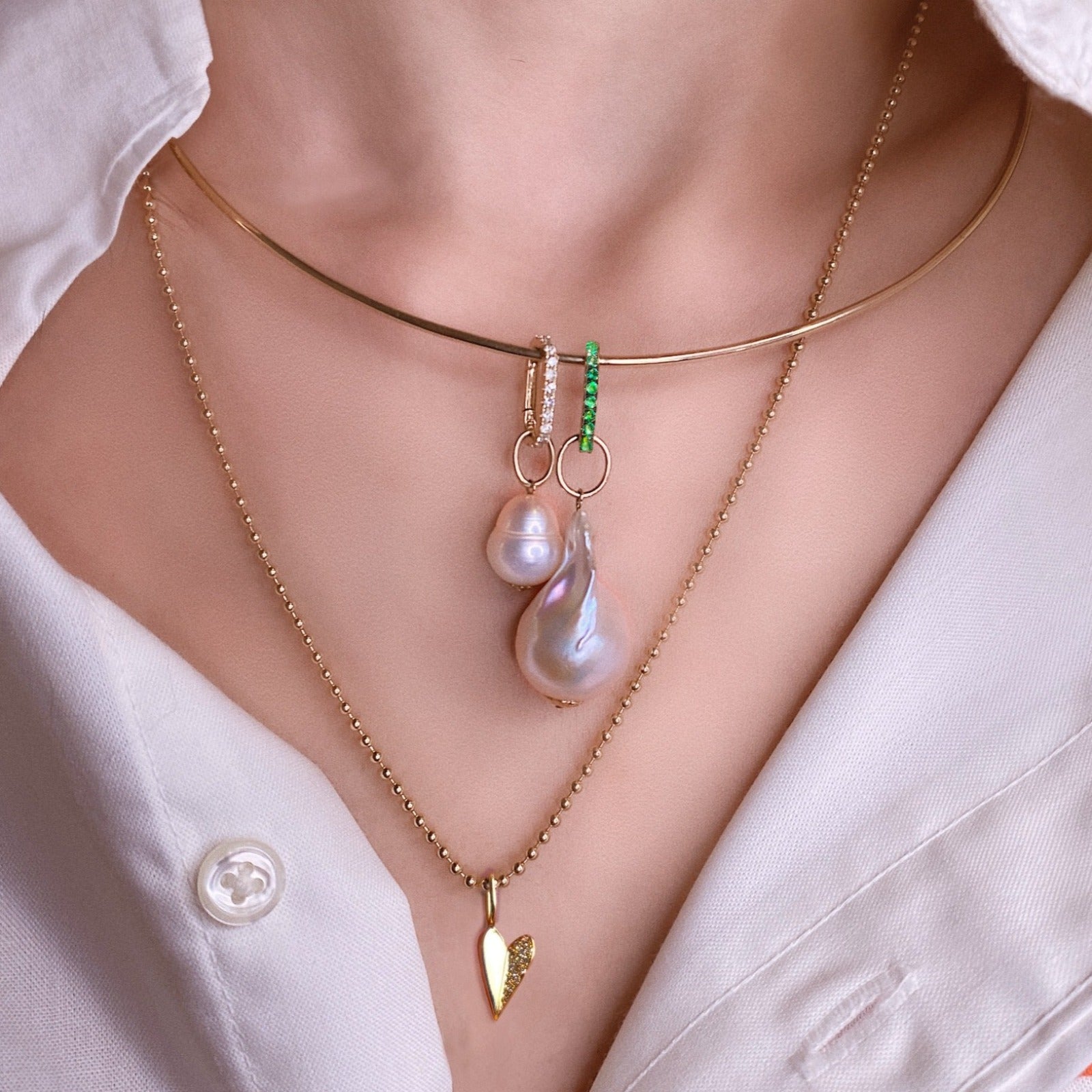 14k yellow gold oval locking charm with green stones styled on a neck locked on a wire choker necklace and mini baroque pearl charm.