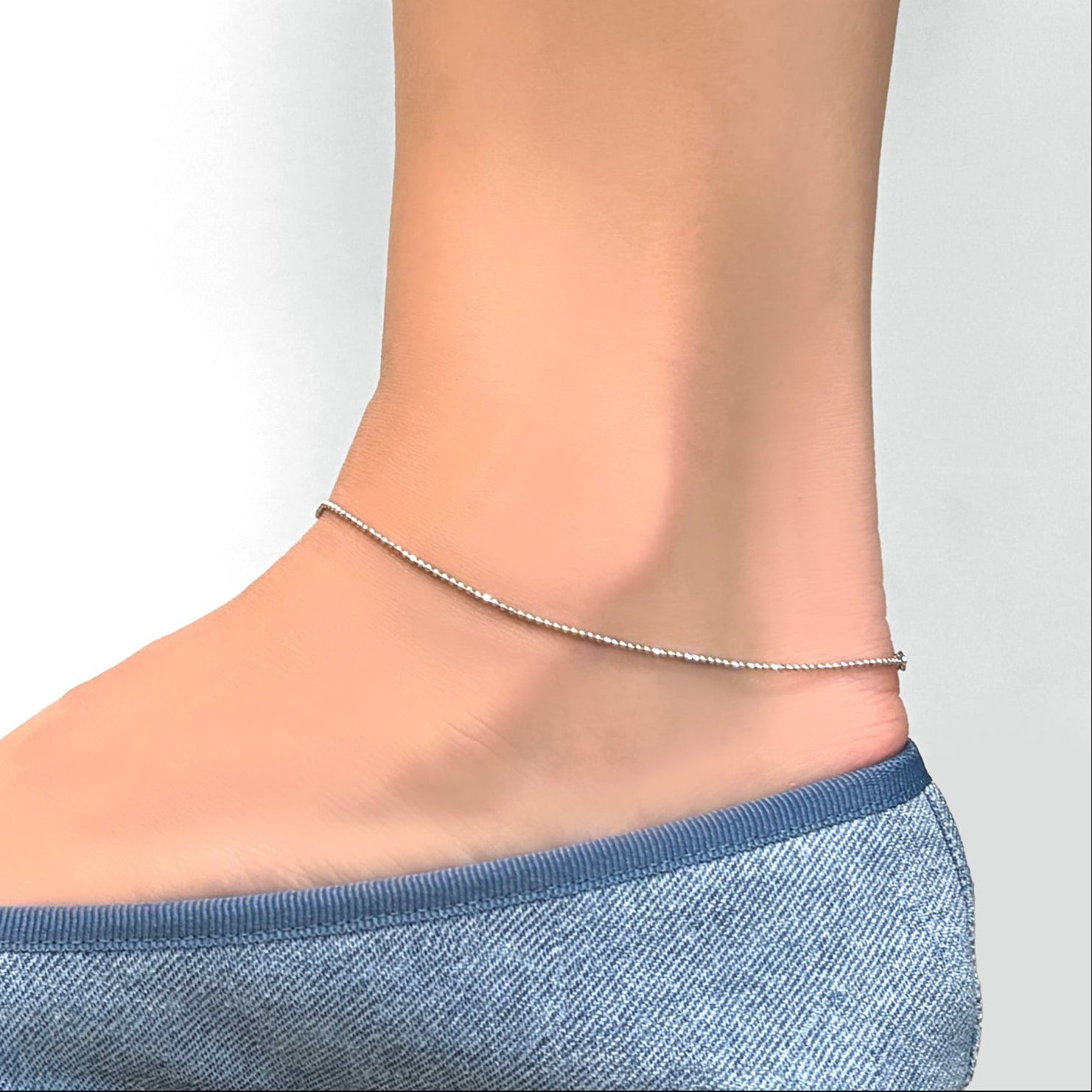 Sterling Silver diamond cut bead chain anklet lon a model's ankle, wearing chambray denim ballet flats.