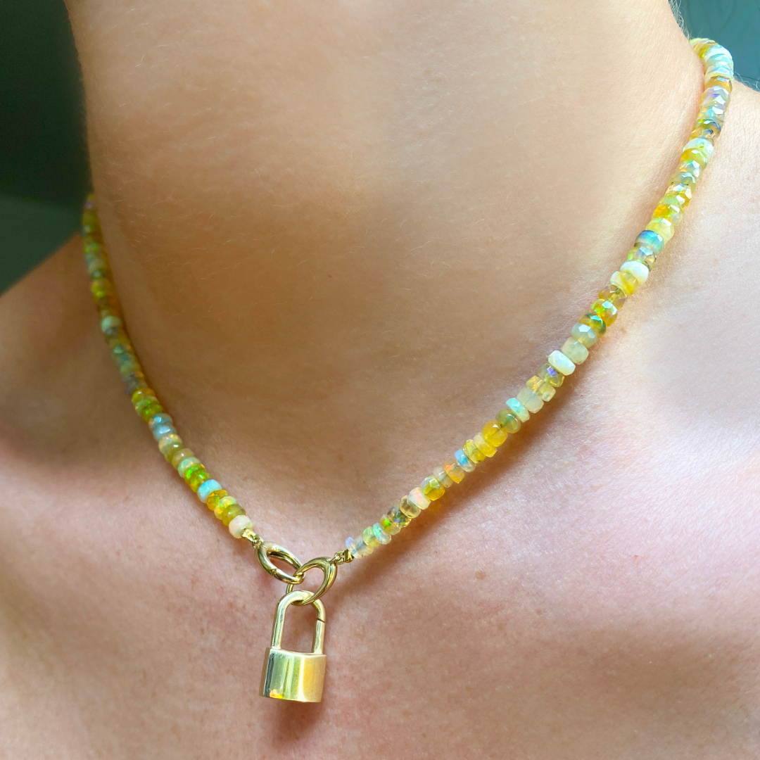14k yellow gold padlock charm. Styled on a neck locked onto oval clasps of a beaded necklace.