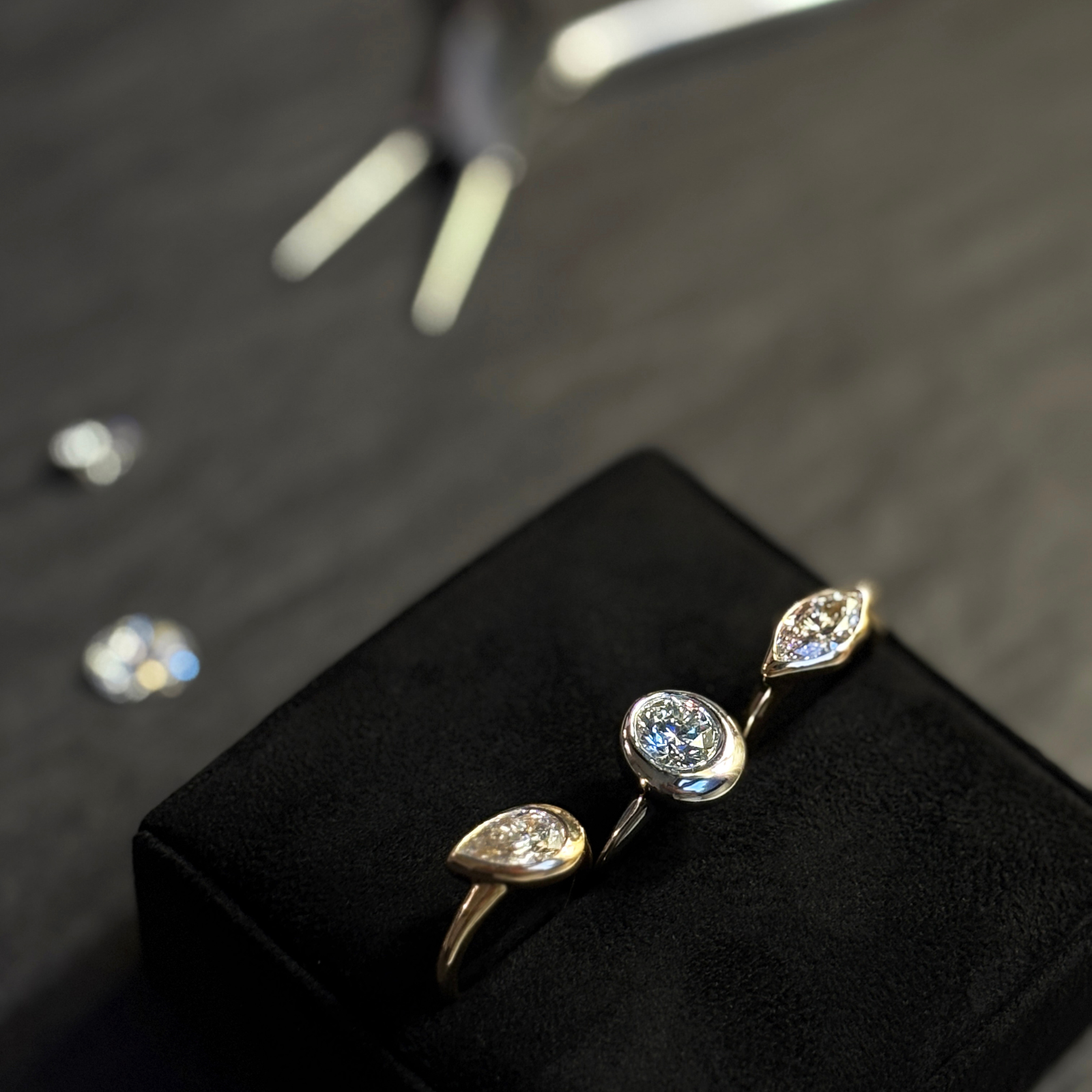 Three AMANDA PEARL rings in 14K recycled yellow and white gold, with lab grown diamonds, sit on a ring cushion with a pair of pliers and l,oose diamonds behind them.