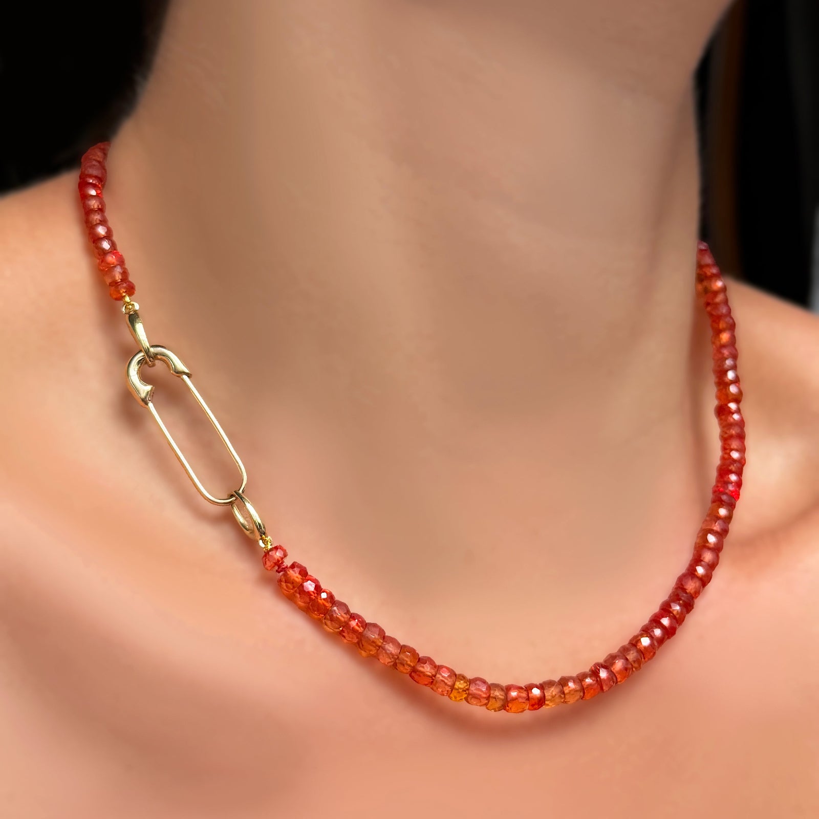 A blood orange faceted padparadscha sapphire necklace with 14k yellow gold molten safety pin charm lock.