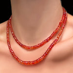 A closeup of two strands of blood orange padparadscha faceted sapphires on a model's neck.