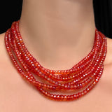 A close-up of a stack of 16" and 18" blood orange faceted padparadscha sapphire necklaces on a model's neck.
