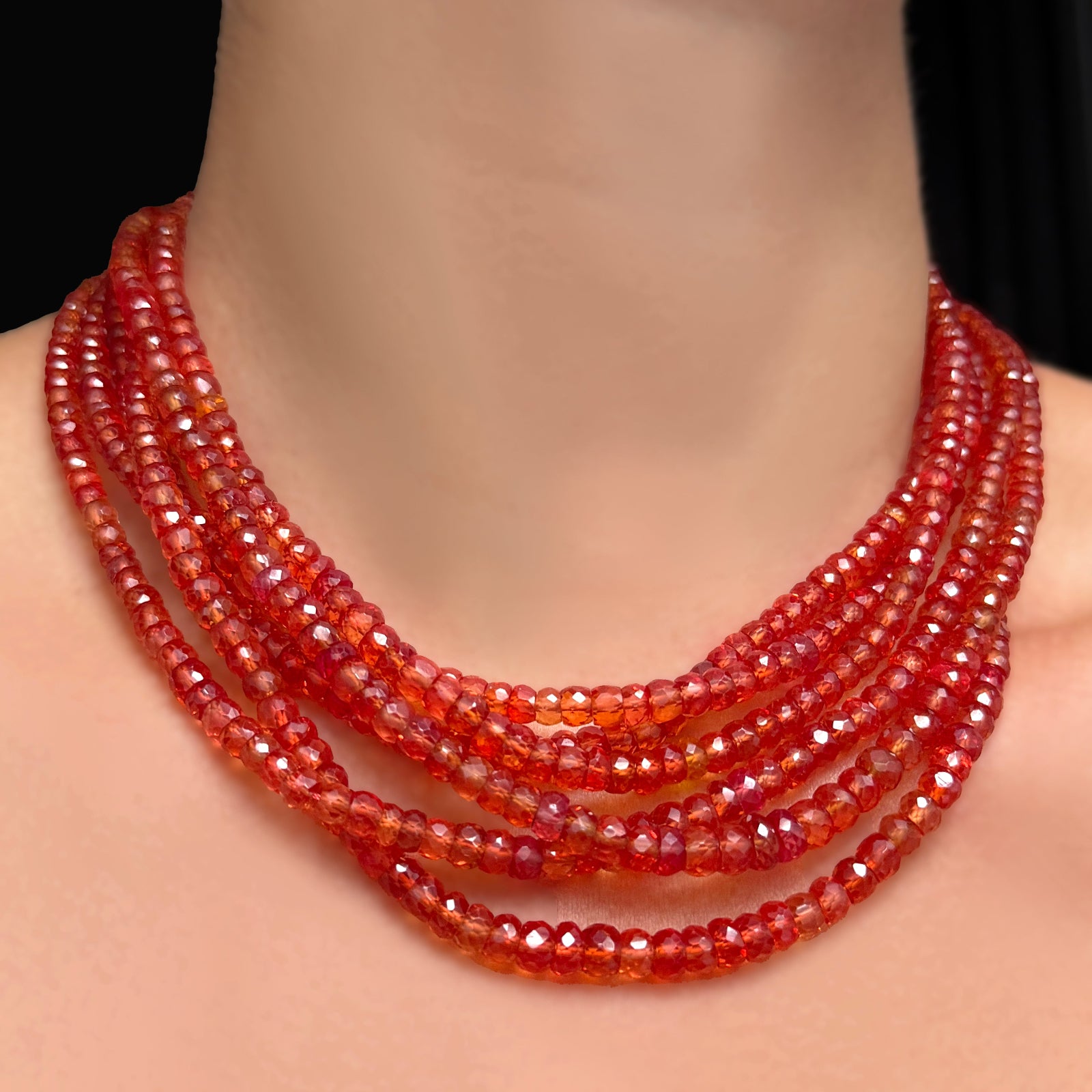 A close-up of a stack of 16" and 18" blood orange faceted padparadscha sapphire necklaces on a model's neck.