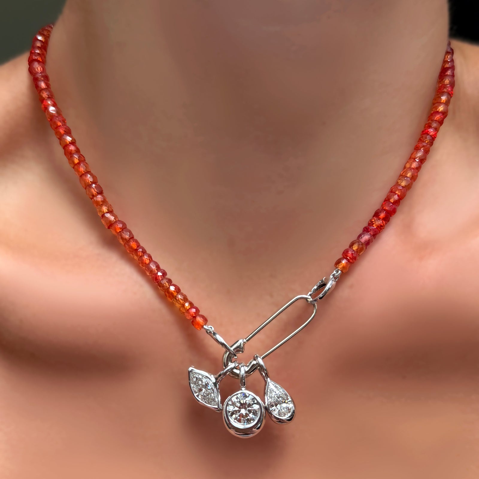 A blood orange padparadscha faceted sapphire necklace with white gold evolution clasp with molten safety pin charm holding a trio of molten solitaire diamond charms.
