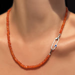 A faceted carnelian necklace on a model's neck with a paperclip charm lock with lapis cabochon.