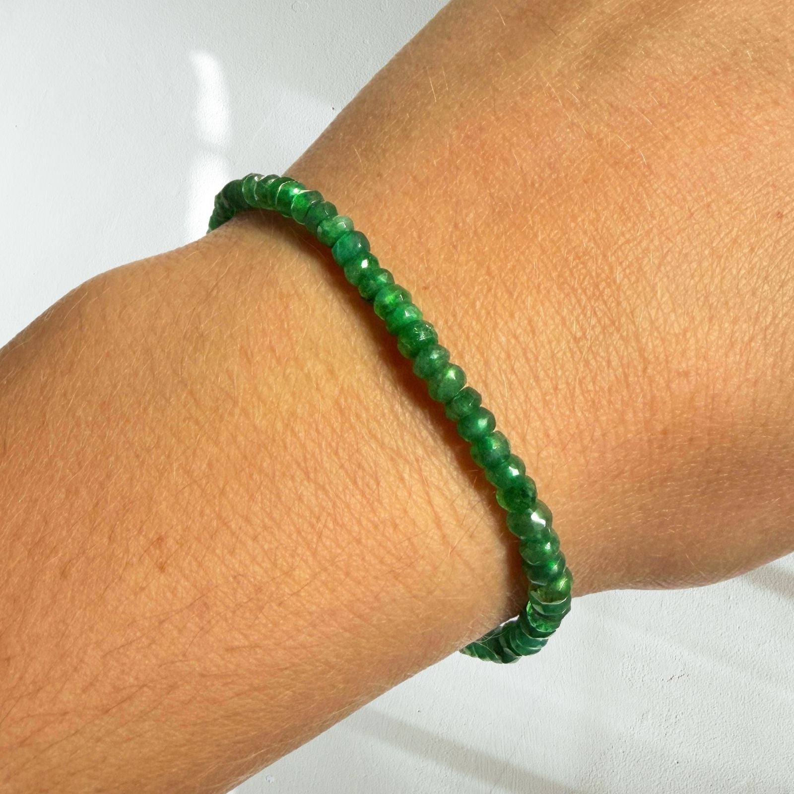 Faceted emerald gemstone beaded bracelet on a model's wrist.