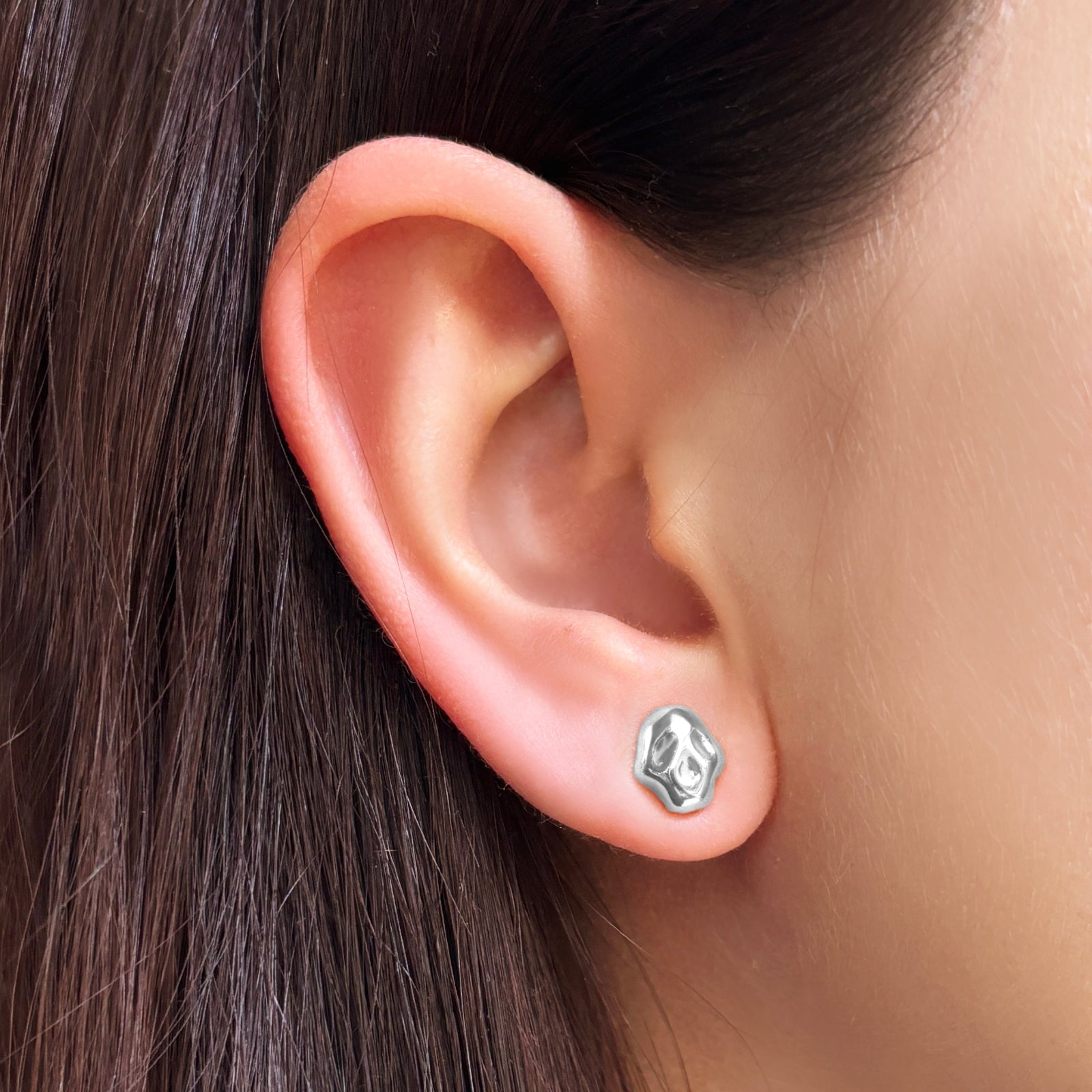 AMANDA PEARL sterling silver molten skull stud earring on a model's ear.