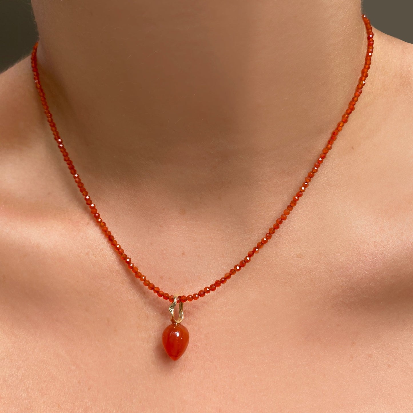 Shimmering beaded necklace made of 2mm faceted opals in shades of orange on a gold linking lobster clasp. Styled on a neck with an acorn drop charm.