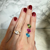 A close-up of a hand with dark red nail polish wearing a 14K yellow gold pear-cut diamond ring, with three alternative colorful gemstones set on her hand. They are peridot, pink topaz, and blue topaz.